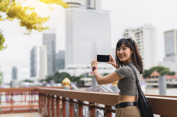 Happy solo southeast asian woman and teenager blogger take photo with smartphone. world travel explorer having local cultural experience for tourism Bangkok Thailand wait for an express boat Chao