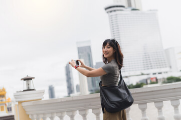 Happy solo southeast asian woman travel blogger take photo with smartphone. world tourism concept and local cultural experience for an explorer on Chao Phraya River in Bangkok Thailand