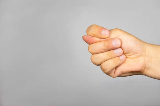 On a gray background, a man's hand with fingers folded in a fig sign
