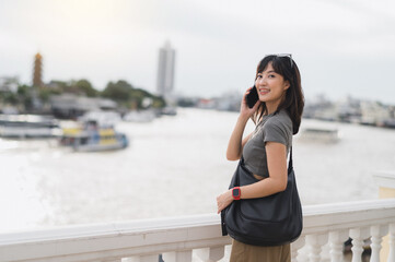 Happy solo Southeast Asian woman and teenager blogger world travel tourism, local cultural experience. Wait for friend and express joy with smartphone by boat Chao Phraya river Bangkok Thailand