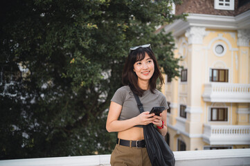 Happy solo southeast asian woman teenager blogger on trip in Bangkok Thailand. joyful tourism travel concept for world explorer using smartphone to express feelings and wait for friend