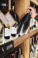Customer selecting a wine bottle from a wooden shelf in a store. Interior of a wine shop with...