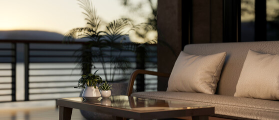 A glass top wooden table and sofa with pillow cushions in a dim lit living room with scenery outside.