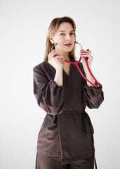 Portrait of a young female doctor in a dark uniform holding a pink stethoscope and looking confidently at the camera on a white background.