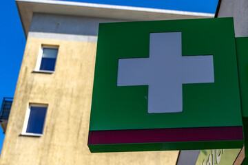 A white cross on a green background on a luminous banner hanging on the facade of a building, a...