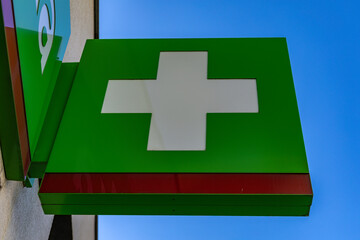 A white cross on a green background on a luminous banner hanging on the facade of a building, a pharmacy, a hospital,