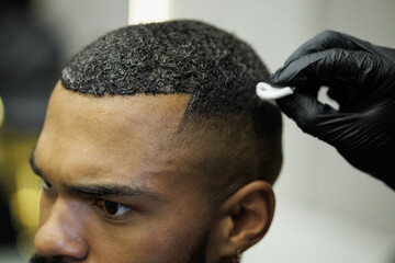 Partial shot of barber wiping off dye from hair of african american client in barbershop