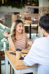 Asian woman smiling and talking explaining to a friend while sits at wooden table in cafe or canteen