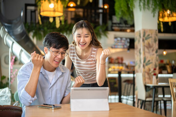 Standing asian woman and sitting man looking happy excite at tablet on wood table in cafe or canteen