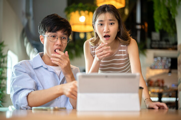 Asian woman and man hand covering mouth in surprise as looking at tablet on table in cafe or canteen