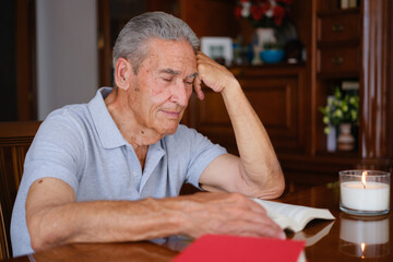 Elderly man smiling while reading at home with a lit candle, sitting at a wooden table in a peaceful and thoughtful atmosphere.