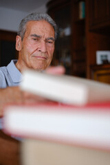 Senior man picking a book in his cozy living room, vertical shot
