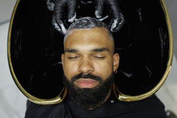 Top view of barber washing hair of african american man with shampoo in barbershop