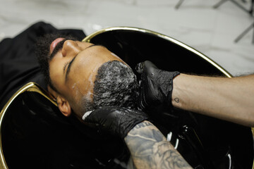 Obraz premium Barber washing hair of african american man in barbershop 