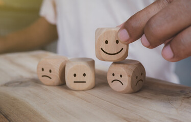 Hand holding wood cube with smile icon, World mental health day or feedback rating concept, Positive customer review, Wood cube stacking with emotion face icon on wood  background