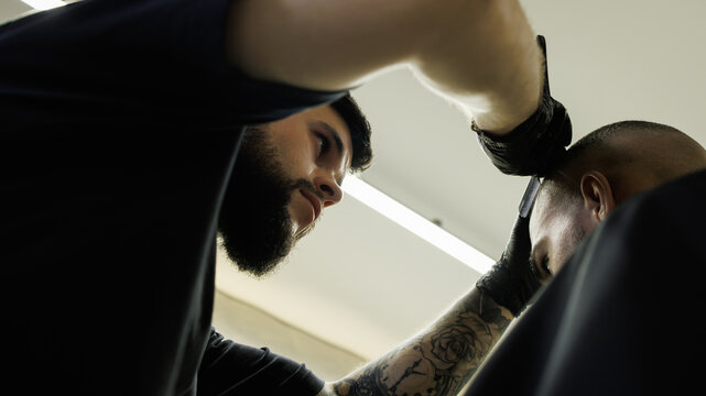 Low angle view of tattooed barber shaving head of african american client 