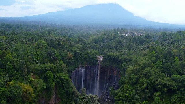 Titel: Aerial drone view of Tumpak Sewu waterfall in Java Island, Indonesia. Stunning panoramic of tropical vegetation with active Semeru volcano in the background..

