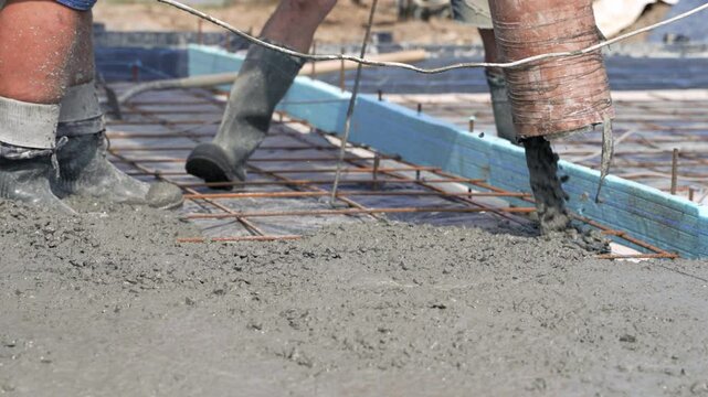 Pouring of a monolithic concrete foundation slab reinforced with an iron grid. Mechanized supply of concrete mix through a pipe. Close-up.