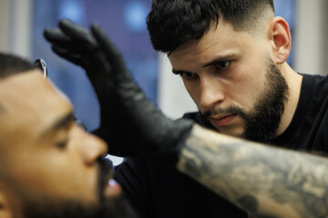 Obraz premium Barber shaving beard of client by using razor in barbershop