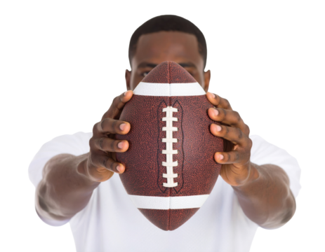 A man wearing a white shirt holds a brown American football directly towards the camera with both hands.