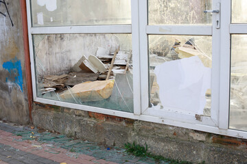 Shattered glass frames a view of a dilapidated interior filled with debris, revealing the neglected...