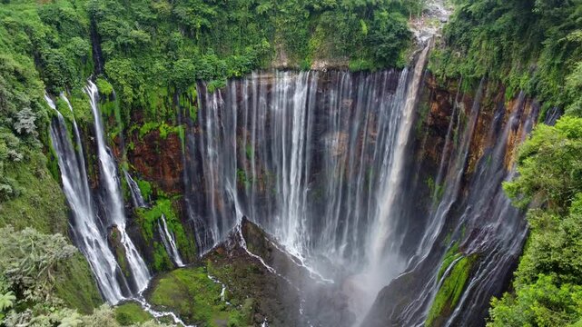 Titel: Aerial drone view of Tumpak Sewu waterfall in Java Island, Indonesia. Stunning panoramic of tropical vegetation with active Semeru volcano in the background..
