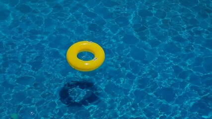 Swimming pool and inflatable ring are peacefully shown as a bright yellow float drifts slowly on clear blue water under the summer sun, creating a relaxing vacation scene and symbolizing leisure, safe