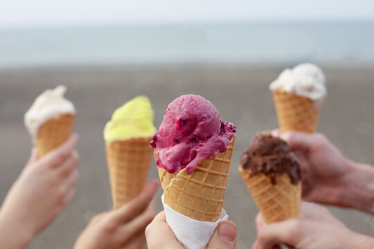 Many hands holding ice cream cones with different  scoops of ice cream on sea beach background. Holiday, vacation and sweet food concept