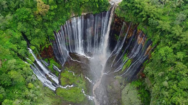 Titel: Aerial drone view of Tumpak Sewu waterfall in Java Island, Indonesia. Stunning panoramic of tropical vegetation with active Semeru volcano in the background..
