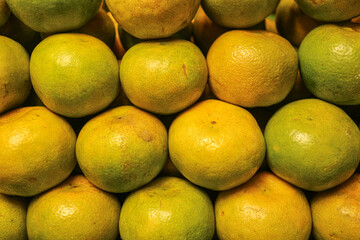 Close up horizontal shot of honey tangerines from Thailand , showing golden yellow and green textured peel , sweet and tangy local street fruit beautifully arranged in a row.