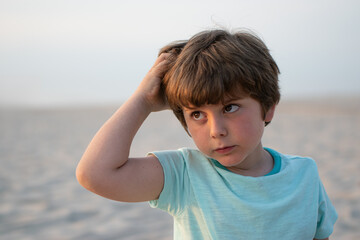 Close-up portrait of a thoughtful boy sitting on a sandy beach during a warm summer evening. Space...
