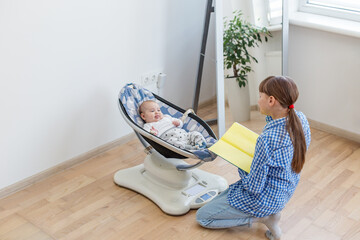 Sister reading book to baby in cradle.