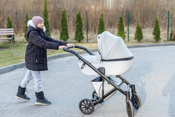 Preteen girl pushing baby stroller outdoors.