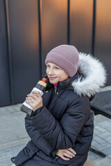 Street food. Smiling girl in winter coat eating hot dog