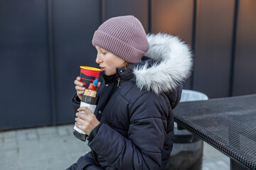 Girl drinking and eating hot dog outside in winter. Street food