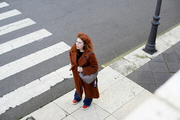 Woman with red hair and brown coat waiting at crosswalk