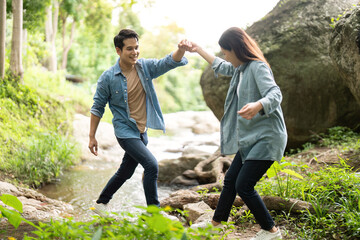 Couple enjoying playful moment while crossing stream. Young man and woman holding hands in nature.