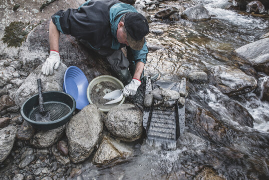 Outdoor adventures on river. Gold panning in a mountain creek, search for gold in winter. Man is looking for gold with a sluice box, sieve, gold pan and shovel