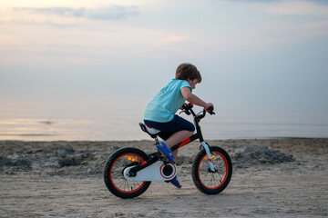 Boy learning to ride a bicycle on a sandy beach at summer sunset