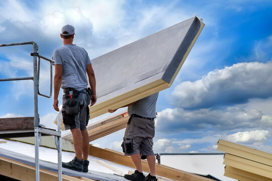 Two construction workers installing large insulation panels on a roof. Energy-efficient renovation, sustainable building practices, and climate protection in the housing sector.