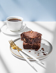 Chocolate brownie with nuts on a plate on a light background with cup of freshly brewed coffee
