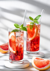 Two glasses of cocktail with grapefruit, mint and ice on marble stand on a light background