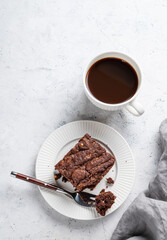 Chocolate brownie on a plate on a light background with cup of freshly brewed coffee and napkin.
