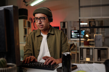 South Asian man wearing headset operating computer in office setting, focusing on screen while...