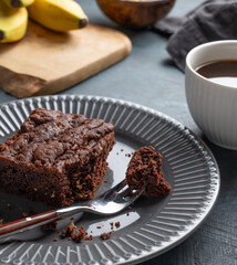 Vegetarian chocolate banana brownie on a plate on a dark background with a cup of coffee
