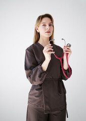 Portrait of a young female doctor in dark medical uniform holding a pink stethoscope and looking confidently at the camera on white background.