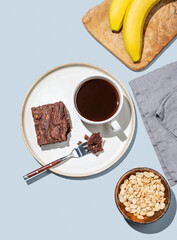 Сhocolate banana brownie on a plate on a blue background with a cup of coffee, nuts and fresh fruits.
