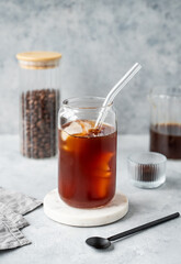 Cold brew coffee in a glass with ice on a marble stand on a light concrete background