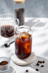 Cold brew coffee in a glass with ice on a light background with coffee beans and morning shadows.