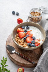 Natural yogurt with granola, blueberry and strawberry in a bowl on a wooden board
